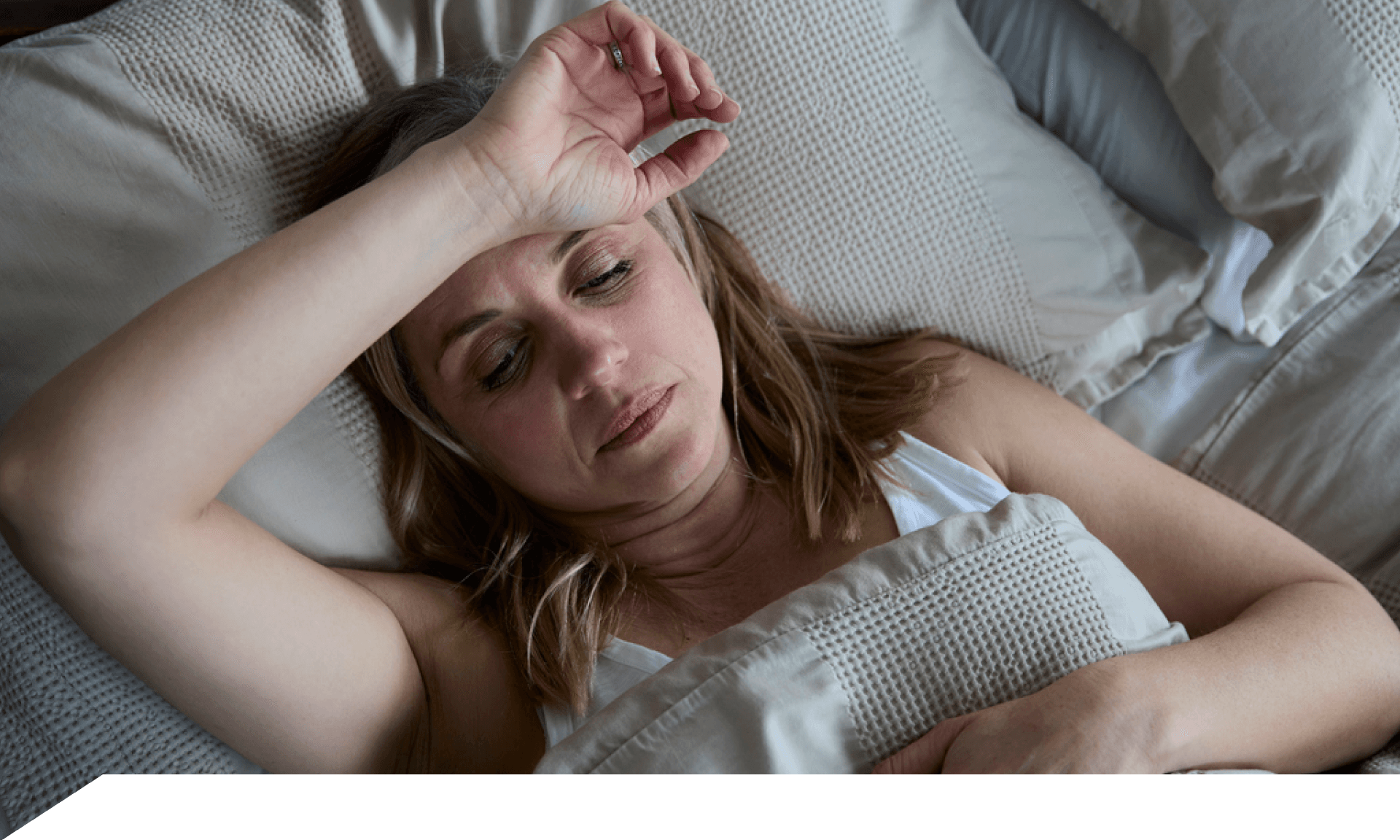 Woman laying on her back in bed with forearm across forehead