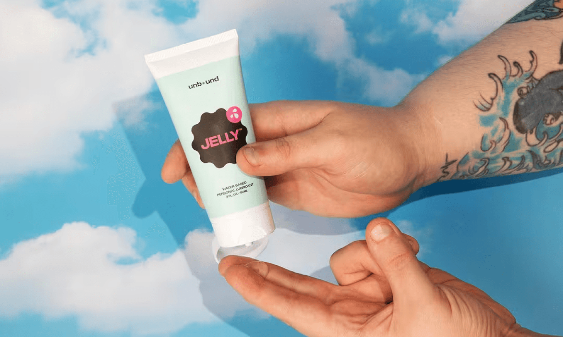 Sage green tube of lube squirting onto set of hands with clouds background