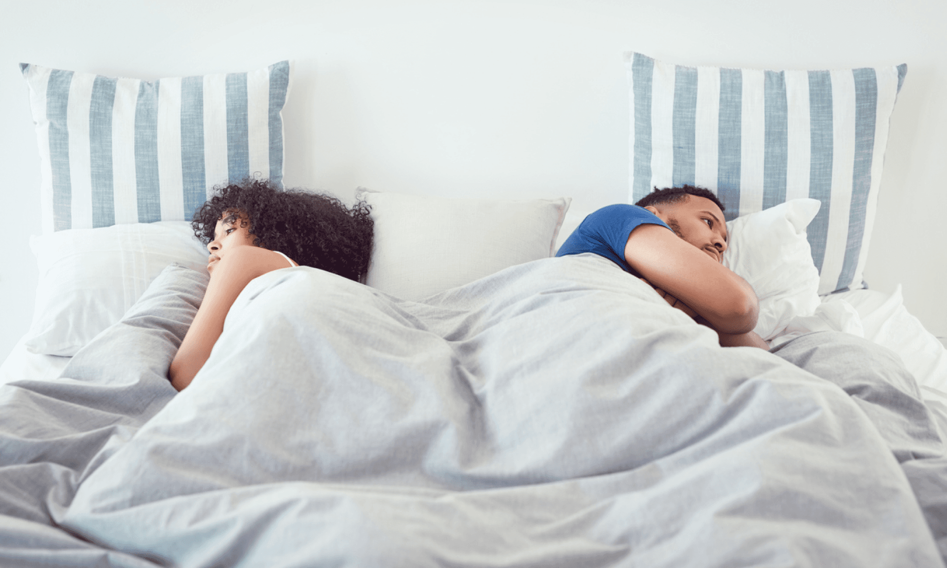 A woman and a man laying in bed, facing away from each other