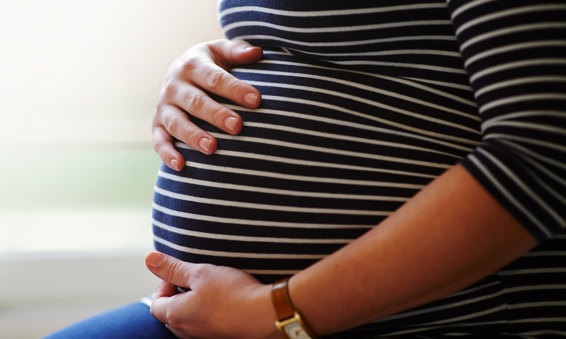 Heavily pregnant female sitting by window, holding her bump with both hands.